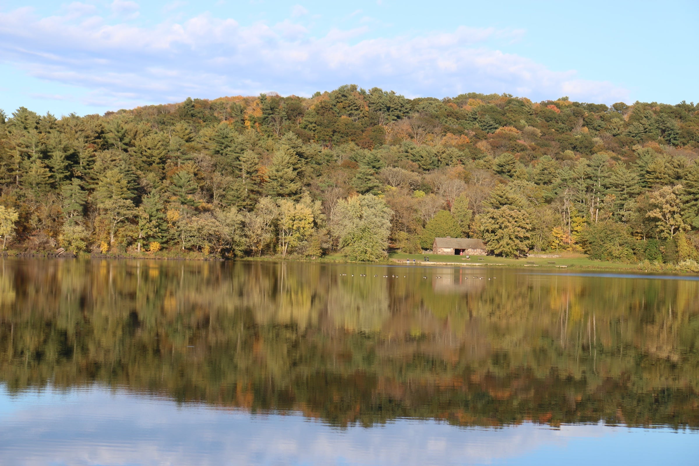 Lake O' the Dalles in Interstate State Park in early fall, with a wooded hillside reflected in still water.