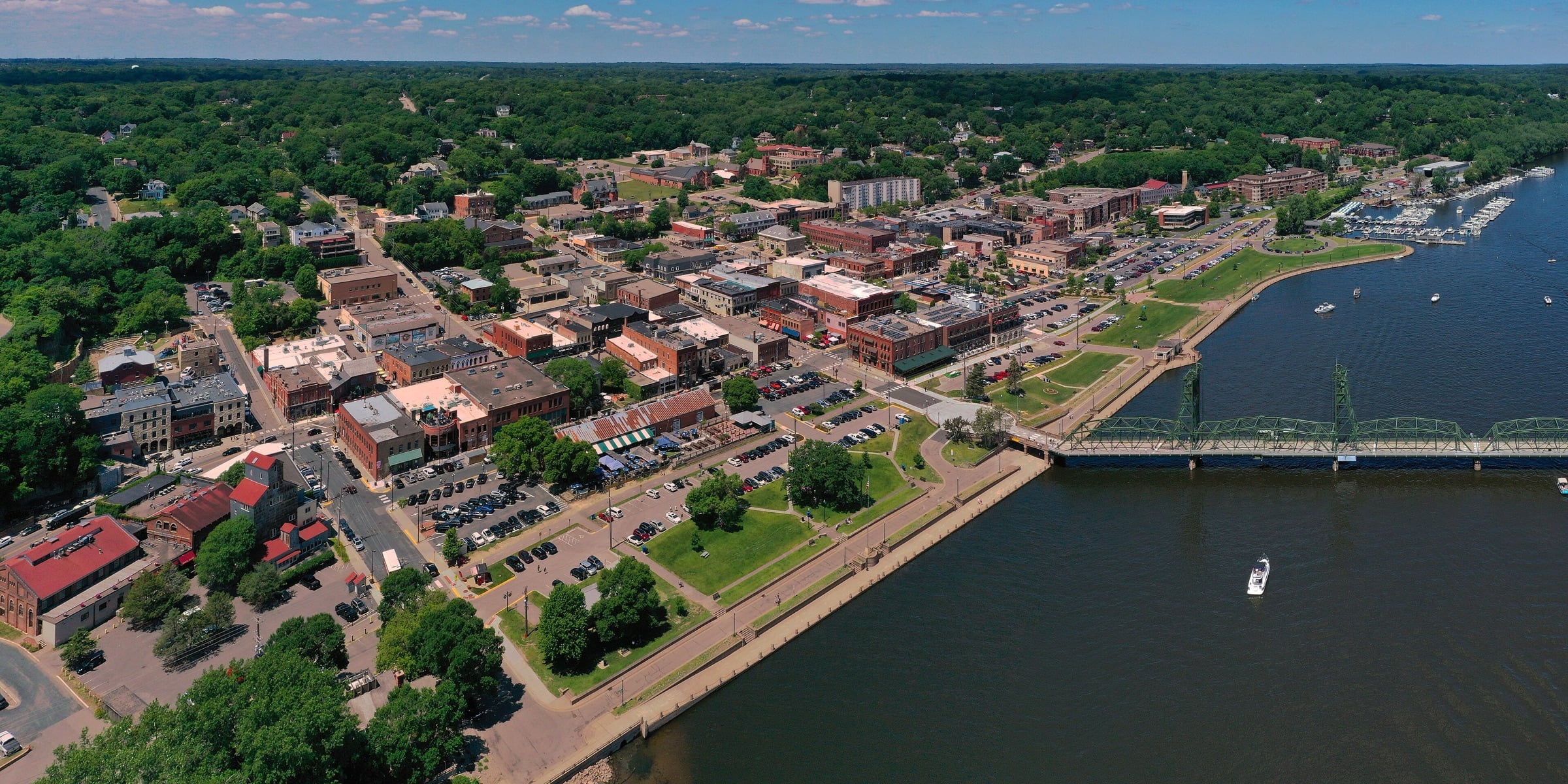 Aerial view of downtown Stillwater along the St. Croix River, with brick buildings, the riverfront park and the Lift Bridge.